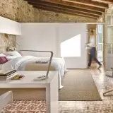 Habitación con cama, escritorio y una persona caminando. Usa paredes falsas para separar espacios, integrando piedra rústica y diseño moderno.