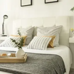 Ideas para como forrar un cabecero de cama: cama con cojines a rayas y lisos, bandeja con desayuno, lámpara y jarrón.