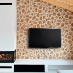 Televisor colgado sobre una pared con un rústico revestimiento de piedra natural, junto a una chimenea moderna.