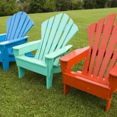 Tres sillas de madera estilo Adirondack, pintadas de azul, verde menta y naranja, lucen vibrantes sobre el césped. ¡Un proyecto de pintar sillas de madera sin lijar que da vida al exterior!
