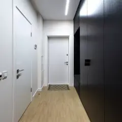 Pasillos estrechos y modernos con puertas blancas y un armario negro. El suelo de madera clara y la iluminación lineal crean un ambiente minimalista.