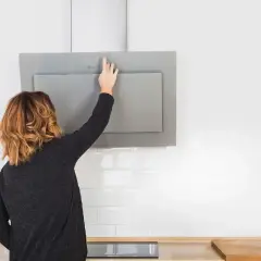 Mujer toca panel de control de campana extractora moderna, lista para cambiarla o limpiarla.