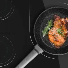 Un filete jugoso se cocina en una sartén sobre una placa de inducción. Aprende como limpiar la placa de inducción para mantenerla impecable.