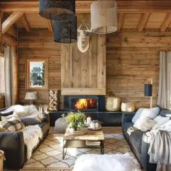 Acogedor salón con chimenea encendida, sofás grises, alfombra de rombos y mucha madera. La decoración casa rústica perfecta para el invierno.