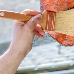 Aplicando el mejor tratamiento para la madera exterior. Una mano con brocha protege la madera, dándole un acabado brillante y duradero.