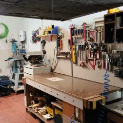 Un completo taller en casa con banco de trabajo, sierra de calar, taladro de columna y herramientas organizadas en la pared.