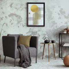 Salón moderno con pared texturizada que combina papel pintado y pintura. Sillón gris, mesa auxiliar dorada y estantería con arte abstracto.