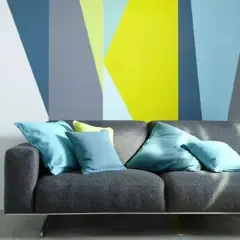 Sofá gris con cojines turques frente a pared con diseño geométrico en colores vivos. ¡Ideas para pintar paredes originales!