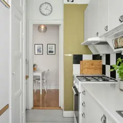 Cocina blanca y ordenada con estantes transparentes para organizar alimentos. Al fondo, un comedor pequeño.