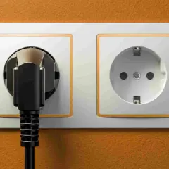 Enchufe negro conectado a una toma de corriente, mostrando partes de un cable con enchufe. Otra toma vacía al lado.