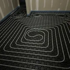 Instalación de tuberías para suelo radiante eléctrico. Se observan las espirales de calefacción sobre una base negra, listas para ser cubiertas.