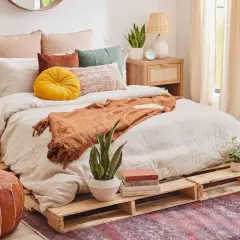 Cama acogedora con cómodas camas hechas con palets, cojines coloridos y manta naranja.