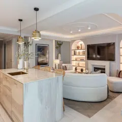 Cocina y sala de estar modernas con isla de mármol, sofás curvos y estanterías iluminadas. La iluminación ambiental crea una atmósfera acogedora, con suficientes **lúmenes por m2** para cada rincón.