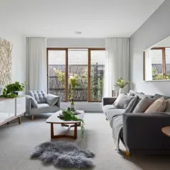 Salón moderno con sofás grises, mesa de centro de madera y arte de pared de ramas. Las paredes color gris crean un ambiente sereno.