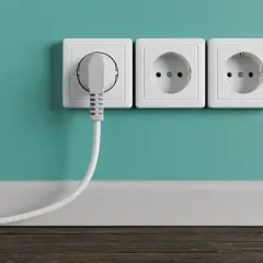 Tres enchufes blancos en una pared turquesa. Uno tiene un enchufe gris conectado. La altura de los enchufes en la cocina es estándar.