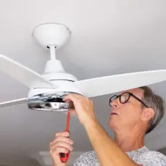 Hombre con gafas ajusta un ventilador de techo pladur con un destornillador.