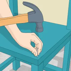 Manos martillando un clavo en una silla de madera azul. Paso a paso, como hacer una silla de madera.