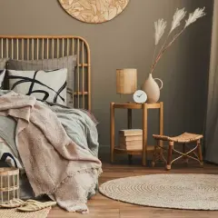 Ideas como decorar una habitación de matrimonio moderna: cama de ratán, ropa de cama con estampado abstracto, manta rosa, alfombra redonda de yute y mesa auxiliar de madera.