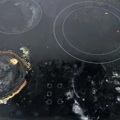 Vitrocerámica con quemada y manchas que no se quitan. Restos de comida y suciedad cubren la superficie, especialmente alrededor de un quemador.
