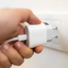 Mano insertando un cargador blanco en un enchufe de pared. Solución fácil de **enchufe sin obra** para cargar dispositivos.