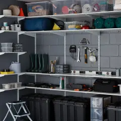 Estanterías metálicas con cajas, herramientas y botas. Una guía visual para saber como organizar un trastero de forma eficiente.