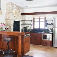 Cocinas con chimenea de piedra, barra de madera con taburetes, electrodomésticos de acero inoxidable y ventana rústica.