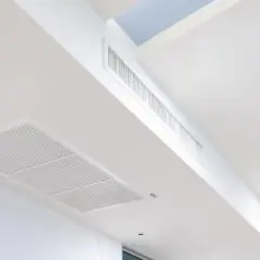 Rejillas de aire acondicionado integradas en un falso techo blanco, con conductos ocultos para una climatización discreta.