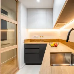 Cocina moderna con puertas de madera y cristal, encimera de madera, fregadero de acero inoxidable y grifo negro. Perfecta para reformas de cocinas pequeñas.