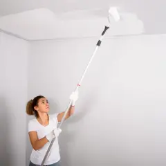 Mujer pintando el techo con rodillo. La pregunta de si que se pinta primero el techo o las paredes se resuelve pintando el techo.