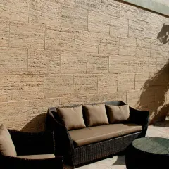Un patio acogedor con muebles de mimbre y cojines marrones, rodeado de patios con paredes de piedra natural.
