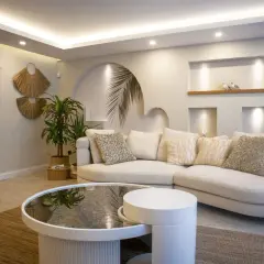 Sofá curvo blanco con cojines texturizados, mesa de centro redonda, y **últimas tendencias iluminación salones** con luces empotradas y perimetrales.