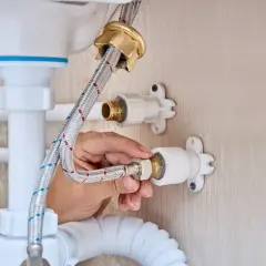 Mano ajustando la conexión de una manguera a la llave de paso de agua general, parte de la fontanería de un lavabo.