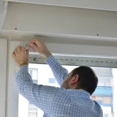 Hombre con camisa a cuadros azules mide con una regla para reparar persiana.
