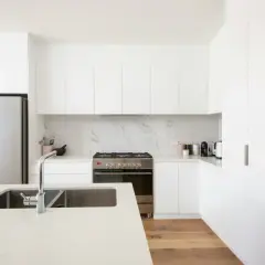 Cocinas modernas blancas con electrodomésticos de acero inoxidable, encimera de cuarzo y suelo de madera.
