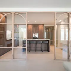 Moderna cocina semiabierta cristal con isla central y taburetes. Muebles de madera oscura y encimera de mármol.