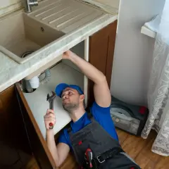 Fontanero trabajando para cambiar grifo cocina. Herramientas y caja de repuestos a mano.