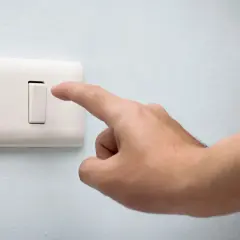 Dedo presionando un conmutador blanco en una pared azul claro.