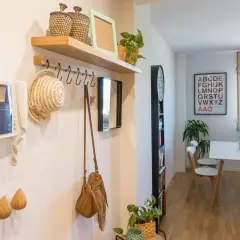 Pasillos con madera en la pared, un perchero con sombrero y bolso, y un intercomunicador. Al fondo, un comedor con mesa y sillas.