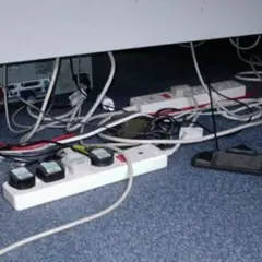 Un enredo de cables y regletas bajo un escritorio. Un ejemplo de qué es un contacto eléctrico indirecto, con cables expuestos y enchufes.