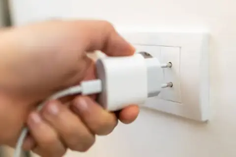 Mano insertando un cargador blanco en un enchufe de pared. Solución fácil de **enchufe sin obra** para cargar dispositivos.
