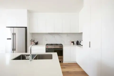 Cocinas modernas blancas con electrodomésticos de acero inoxidable, encimera de cuarzo y suelo de madera.