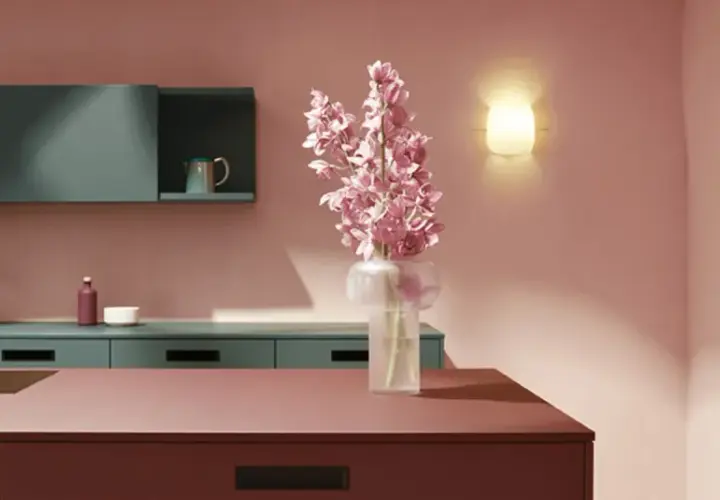 Elegante cocina con una **combinación de colores para cocina** audaz: rosa empolvado, verde azulado y detalles en burdeos y ocre. Flores rosas en un jarrón.