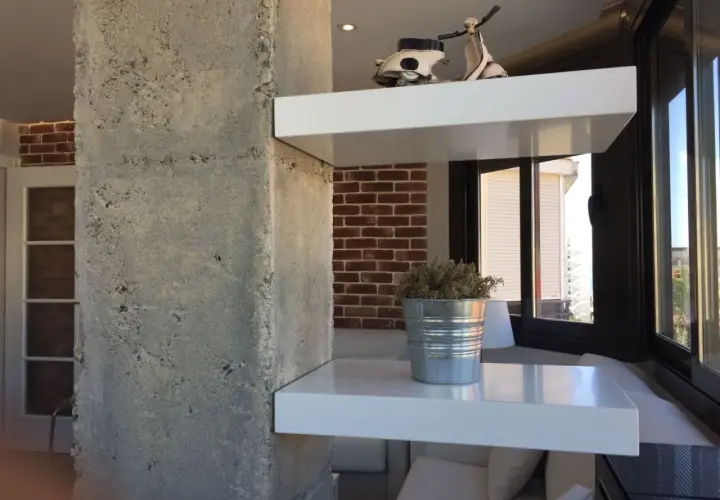 Ideas para decorar columnas dentro de la casa: estantes blancos flotantes con un modelo de Vespa y una planta en lata.