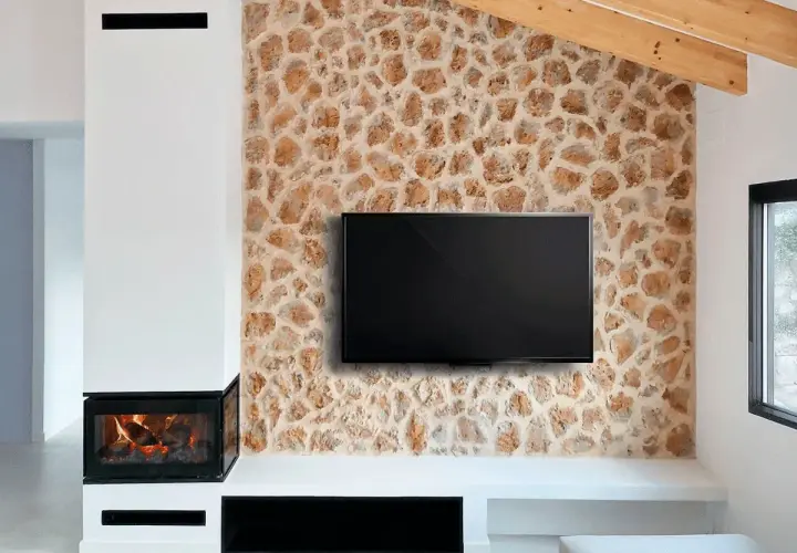 Televisor colgado sobre una pared con un rústico revestimiento de piedra natural, junto a una chimenea moderna.