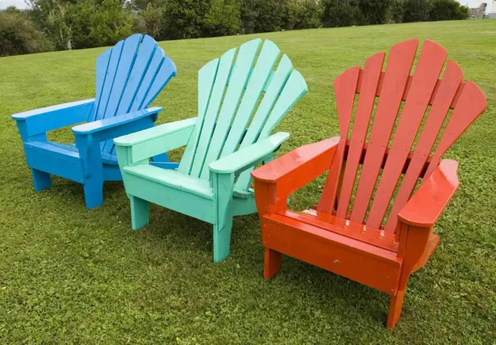 Tres sillas de madera estilo Adirondack, pintadas de azul, verde menta y naranja, lucen vibrantes sobre el césped. ¡Un proyecto de pintar sillas de madera sin lijar que da vida al exterior!