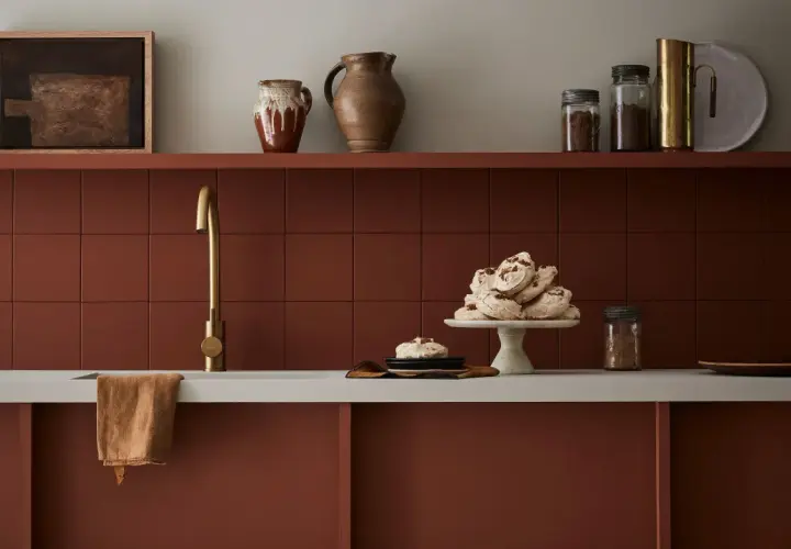 Encimera de cocina pintada en tono terracota, con grifería dorada y detalles decorativos.