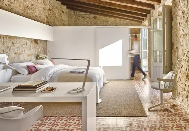 Habitación con cama, escritorio y una persona caminando. Usa paredes falsas para separar espacios, integrando piedra rústica y diseño moderno.