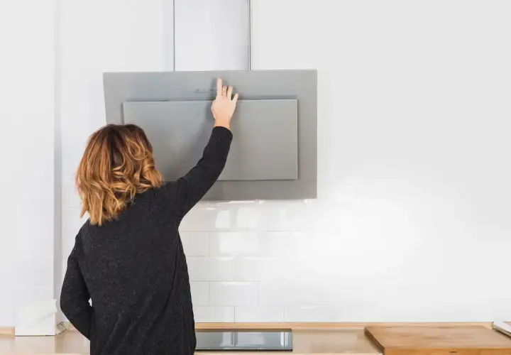 Mujer toca panel de control de campana extractora moderna, lista para cambiarla o limpiarla.