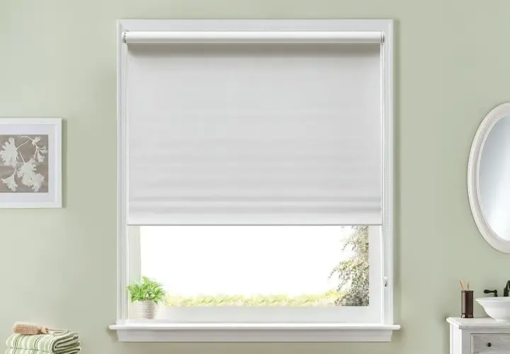 Ventana con estor enrollable blanco, ideal para aprender cómo hacer un estor. Al lado, un cuadro y toallas.