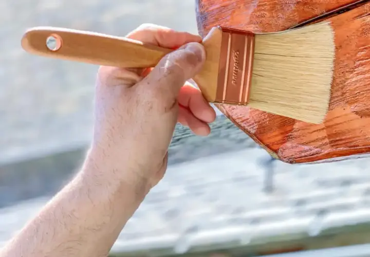 Aplicando el mejor tratamiento para la madera exterior. Una mano con brocha protege la madera, dándole un acabado brillante y duradero.